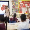Teacher pointing at pupil with his hand up in classroom